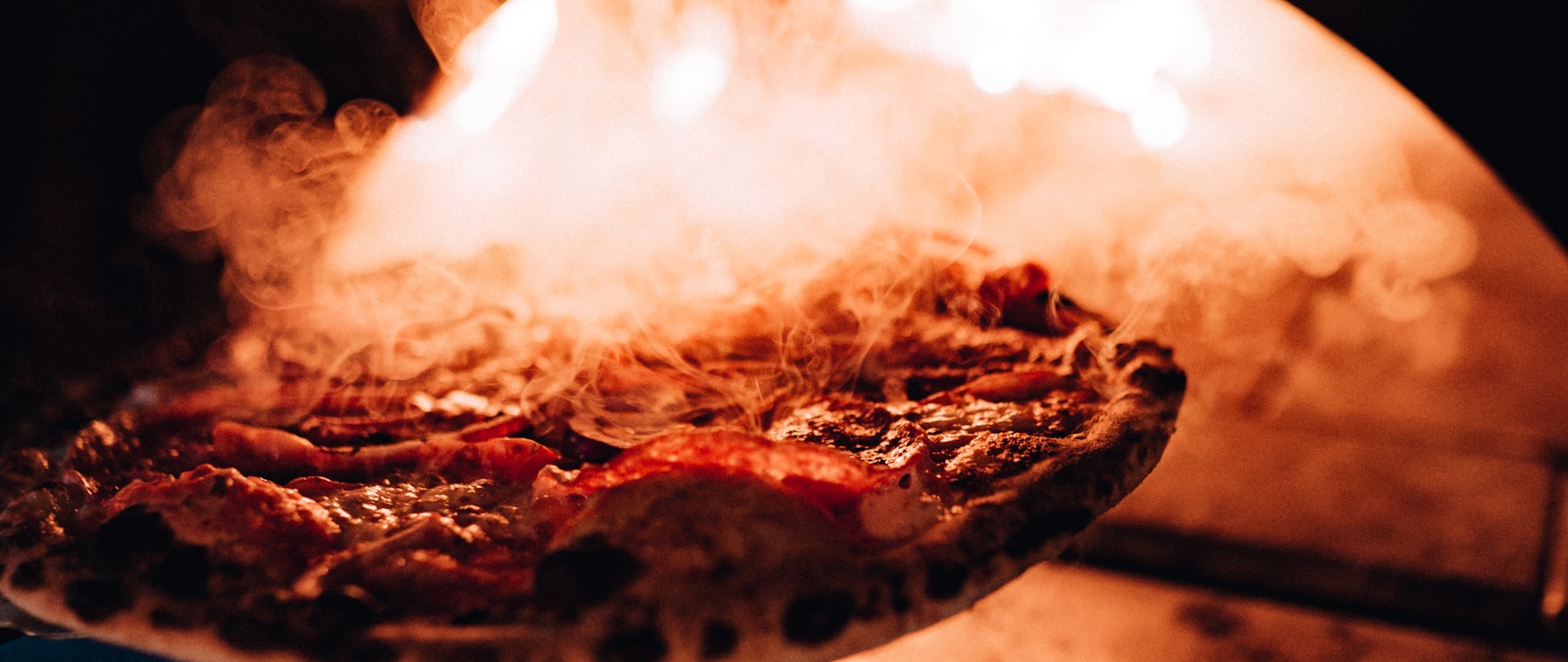 Pizza a kemence lángjai előtt, füstölgő tetején